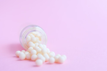 homeopathic globules and glass bottle close up on pink background. Alternative Homeopathy medicine herbs, healtcare and pills concept. Flatlay. copyspace for text