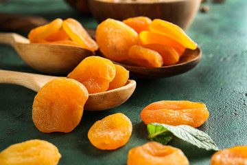 Spoons with dried apricots on color background