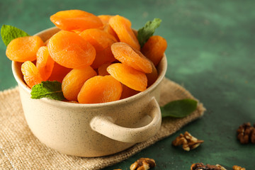 Pot with dried apricots on color background
