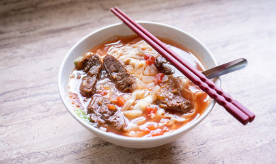 Beef noodle ramen meal with tomato sauce broth in bowl on bright wooden table, famous chinese style food in Taiwan, close up, top view, copy space