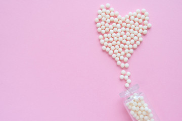 Heart made of homeopathic globules and glass bottle on pink background. Alternative Homeopathy medicine herbs, healtcare and pills concept. Flatlay. Top view. copyspace for text