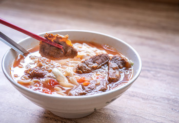 Beef noodle ramen meal with tomato sauce broth in bowl on bright wooden table, famous chinese style food in Taiwan, close up, top view, copy space