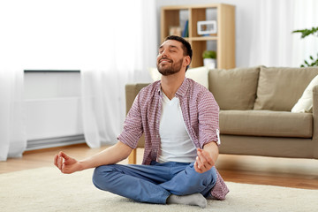 mindfulness, meditation and relaxation concept - man meditating in lotus pose at home