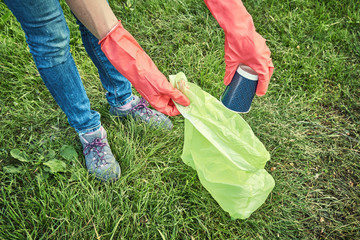 Young  girl picking up the garbage and putting it in a garbage bag on a natural background.