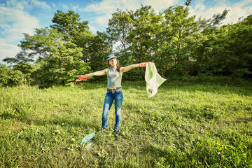 Young  girl picking up the garbage and putting it in a garbage bag on a natural background.