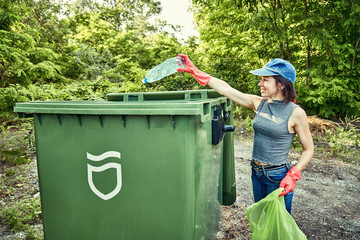 Young  girl picking up the garbage and putting it in a garbage bag on a natural background.