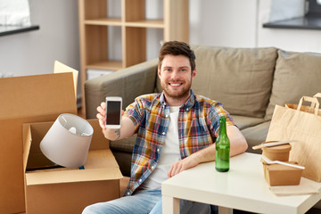 Fototapeta na wymiar moving, food delivery and technology concept - smiling man with smartphone and takeaway lunch at new home