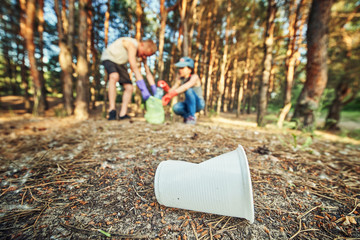 Young  girl picking up the garbage and putting it in a garbage bag on a natural background.