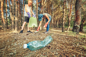 Young  girl picking up the garbage and putting it in a garbage bag on a natural background.