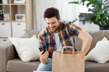 technology, consumption and people concept - smiling man using smartphone for food delivery at home