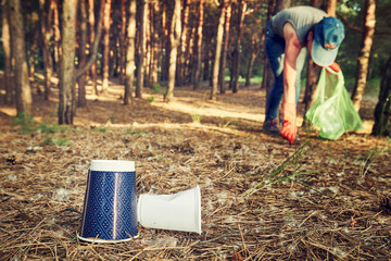Young  girl picking up the garbage and putting it in a garbage bag on a natural background.