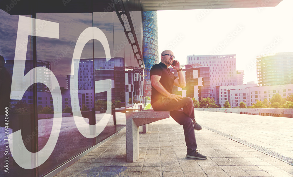 Wall mural young businessman using a smartphone with the new 5g mobile network. urban scene in the street and e