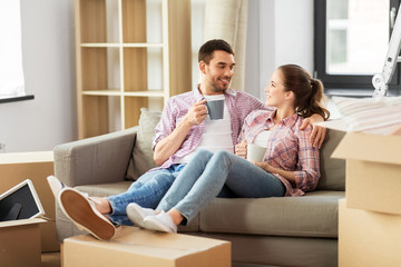 Fototapeta na wymiar moving, people, repair and real estate concept - happy couple sitting on sofa and drinking coffee at new home
