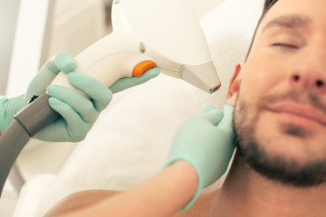 Close up of laser hair removal tool near the ear of man