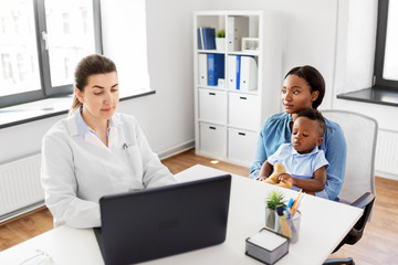 Obraz premium medicine, healthcare and pediatry concept - african american mother with baby son and caucasian doctor with laptop computer at clinic