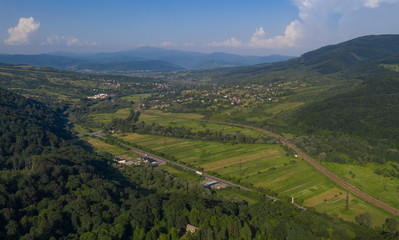 Aerial view of the Carpathian mountains. Natural background with geometric pattern - beige and red rectangles of the fields and roofs and lines of roads and trees. Zakarpattia, Ukraine.