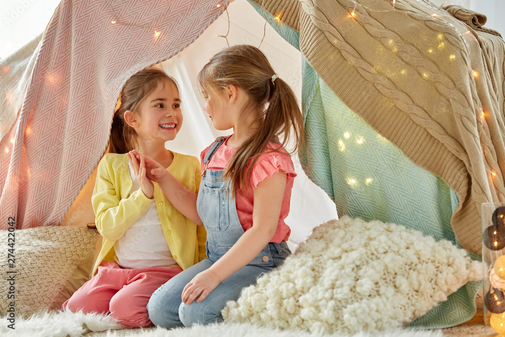 Wall mural childhood, hygge and friendship concept - little girls talking in kids tent or teepee at home