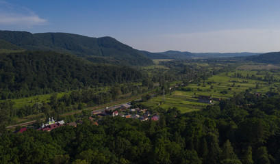 Aerial view of the Carpathian mountains. Natural background with geometric pattern - beige and red rectangles of the fields and roofs and lines of roads and trees. Zakarpattia, Ukraine.