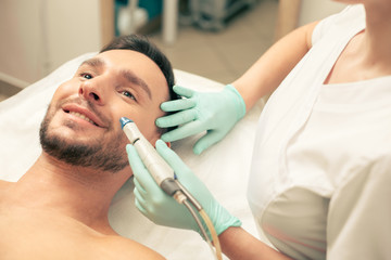 Man smiling and cosmetologist treating his face skin