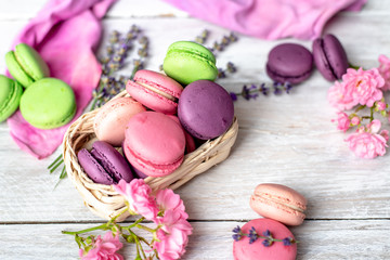 green, lilac, coral and purple macaroons with the addition of rose and lavender flowers, and a pink-purple cotton kitchen cloth on a white, rustic background.