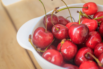 sweet cherry berries in a white plate on a wooden background. Ripe red berries.