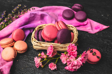 lilac, coral and purple macaroons with the addition of rose and lavender flowers, and a pink-purple cotton kitchen cloth on a dark, rustic background.