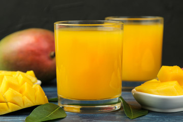 Ripe fresh mango fruit and slices and mango juice in a glass on a blue wooden table. tropical fruit.