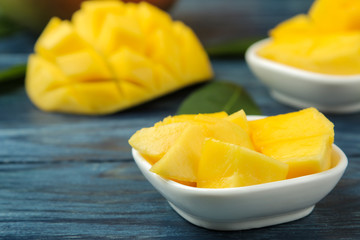 Ripe fresh mango fruit in a basket and slices and leaves on a blue wooden table. tropical fruit.