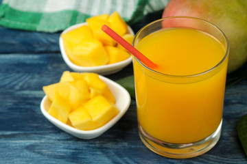 Naklejka na ściany i meble Ripe fresh mango fruit and slices and mango juice in a glass on a blue wooden table. tropical fruit.