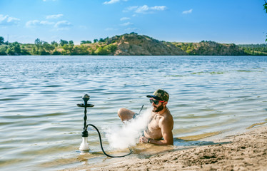 The guy smokes a hookah right in the water on the beach.