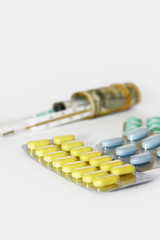 multi-colored medicinal pills, thermometer, syringe and dollars