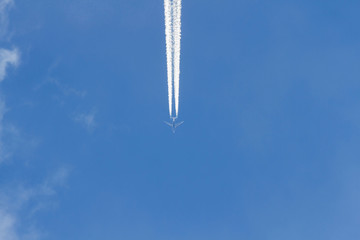 Avion a reaccion volando en el cielo azul. Dejando rastro estela o chorro de vapor de agua, visto desde abajo en plano nadir - obrazy, fototapety, plakaty