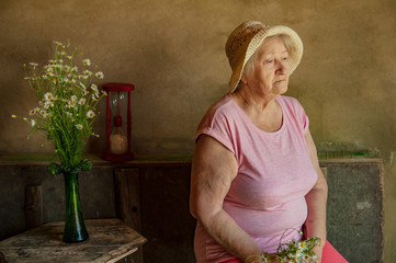 Elderly woman with bouquet of medical daisies in pink T-shirt and hat. Pensioner engaged in...