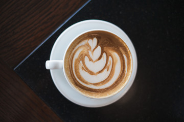 Cup of cappuccino with latte art on black table background.