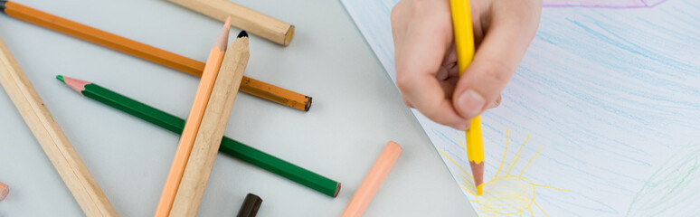 panoramic shot of kid drawing with yellow pencil on paper