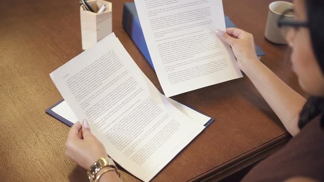 African-american entrepreneur in eyeglasses reading contract in office. Partnership legal agreement draft checking after negotiation. Slow motion.