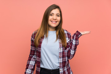 Young girl over pink wall holding copyspace imaginary on the palm to insert an ad