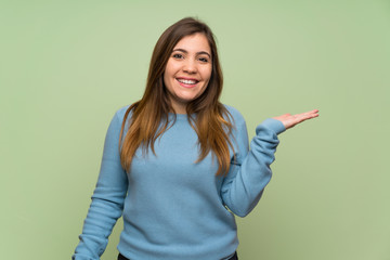 Young girl over green wall holding copyspace imaginary on the palm to insert an ad