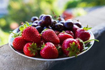 Organic sweet cherry and strawberry on a white plate.