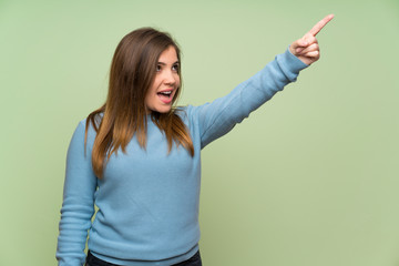 Young girl over green wall pointing away