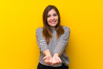 Obraz premium Young girl over yellow wall holding copyspace imaginary on the palm to insert an ad