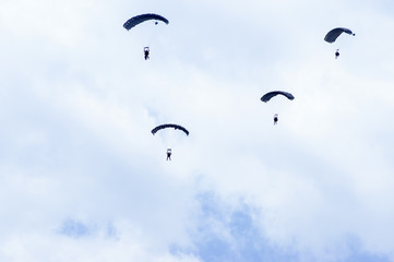 Military parachutists also called paratroopers in the sky with many clouds.