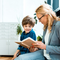 attractive woman in glasses sitting and reading book with happy kid
