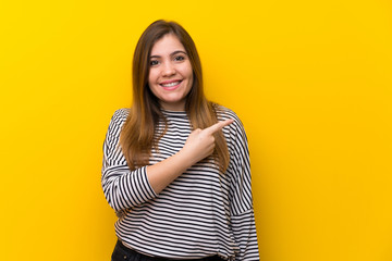 Fototapeta premium Young girl over yellow wall pointing to the side to present a product