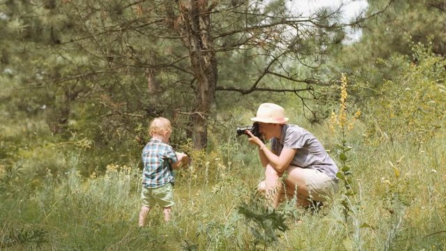 Woman making photo of kid boy during picnic at forest. Mom photographing son, playing and having fun outdoors on nature vacation. Mother taking picture of her cute little child in hat the park.