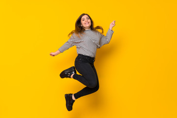 Fototapeta na wymiar A full-length shot of a Young girl jumping over isolated yellow background