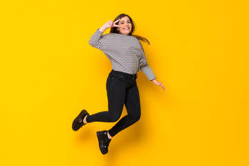 Fototapeta na wymiar A full-length shot of a Young girl jumping over isolated yellow background