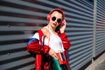 Back in time 90s 80s. Stylish girl in retro jacket and vintage cassette player listens to music, fashion trends, entertainment, heat in summer