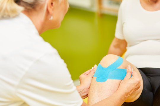 Physiotherapeutin befestigt ein Kinesio Tape am Knie