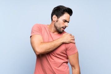 Handsome young man in pink shirt over isolated blue background suffering from pain in shoulder for...